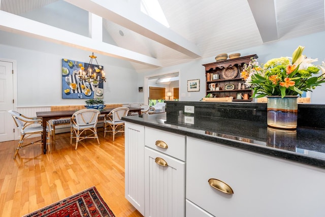 kitchen with white cabinetry, light wood-type flooring, dark stone countertops, vaulted ceiling with beams, and pendant lighting