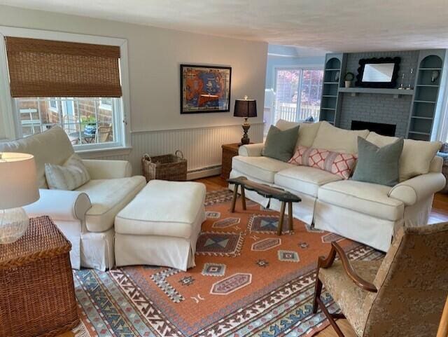 44 Leeward Run, South Yarmouth, MA 02664 - living room with a baseboard heating unit, wood finished floors, wainscoting, plenty of natural light, and a brick fireplace