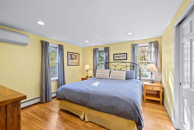 bedroom featuring multiple windows, a wall mounted AC, and light hardwood / wood-style flooring