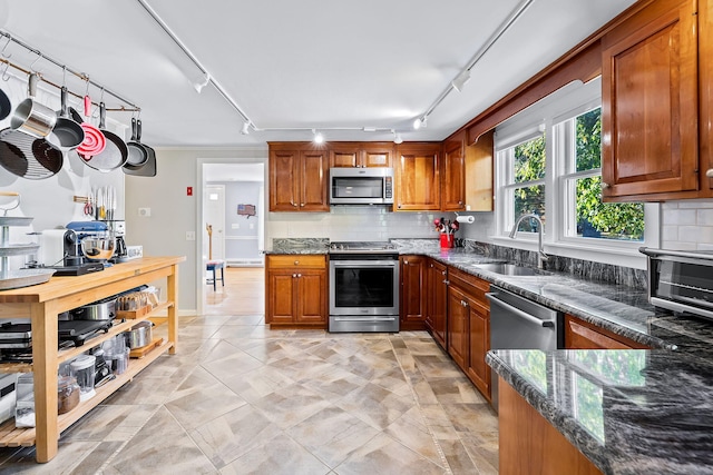 kitchen featuring sink, appliances with stainless steel finishes, dark stone countertops, track lighting, and decorative backsplash