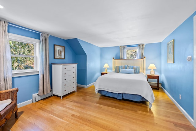 bedroom featuring multiple windows, a baseboard heating unit, and light hardwood / wood-style floors