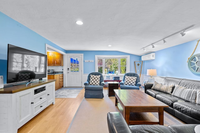 living room with a wall unit AC, light hardwood / wood-style floors, and a textured ceiling