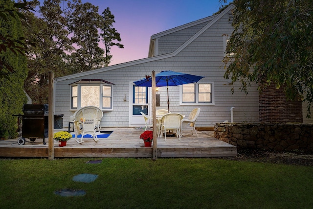 back house at dusk featuring a deck and a lawn