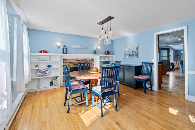 dining area featuring light hardwood / wood-style floors, a brick fireplace, and a baseboard heating unit