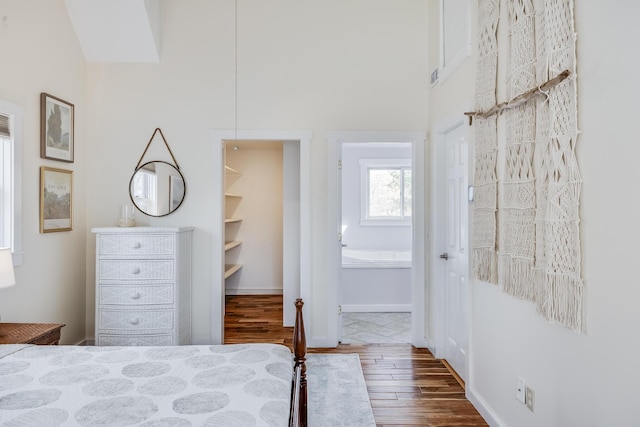 bedroom featuring wood finished floors, ensuite bath, a high ceiling, and a closet