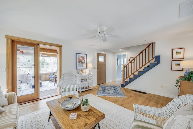 living area with stairs, baseboards, light wood finished floors, and a ceiling fan