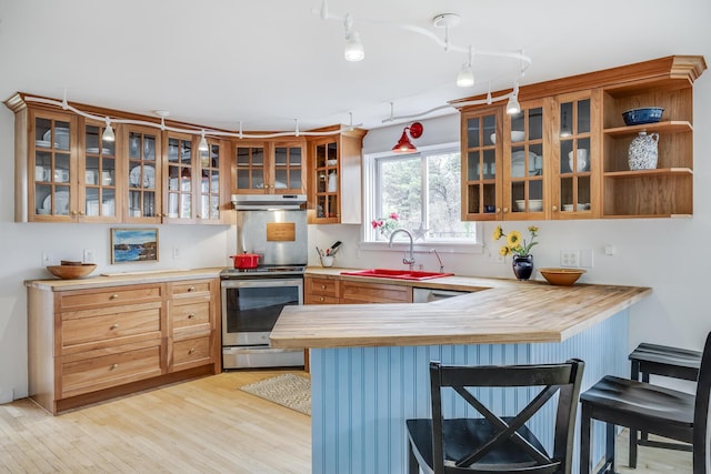 kitchen featuring stainless steel range with electric cooktop, a sink, under cabinet range hood, a breakfast bar, and a peninsula