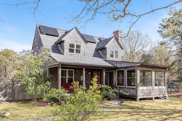 view of front of home featuring a sunroom, roof with shingles, solar panels, a chimney, and fence