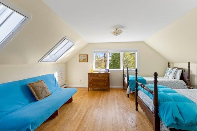 bedroom featuring light hardwood / wood-style floors, baseboard heating, and lofted ceiling with skylight