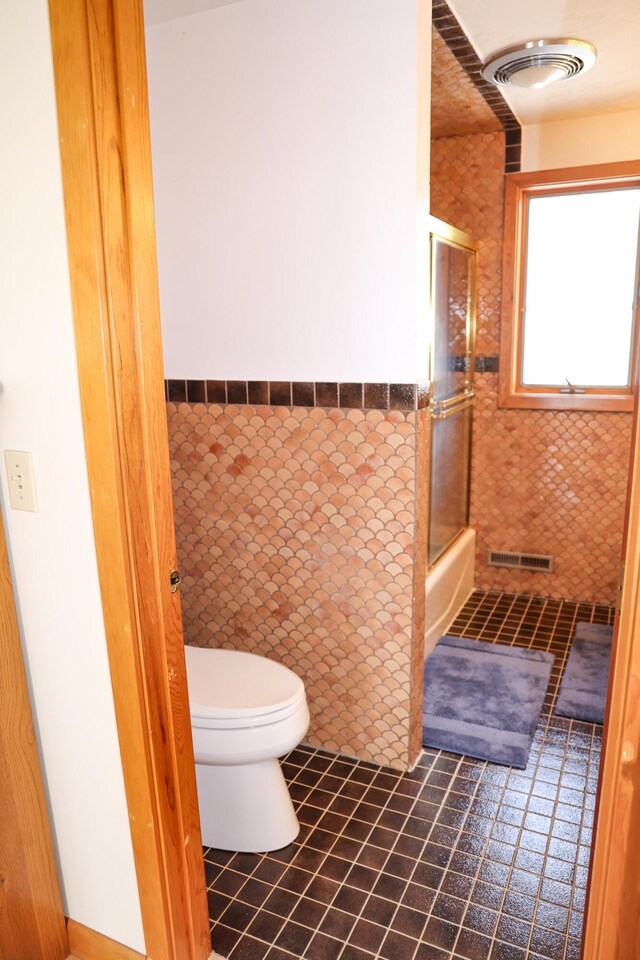 bathroom with visible vents, tile walls, a wainscoted wall, toilet, and enclosed tub / shower combo