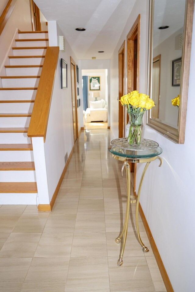 corridor featuring baseboards, visible vents, light tile patterned floors, and stairway