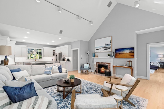 living room with visible vents, high vaulted ceiling, rail lighting, and light wood-style floors