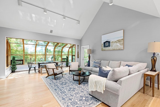 living room featuring rail lighting, plenty of natural light, high vaulted ceiling, and light wood finished floors