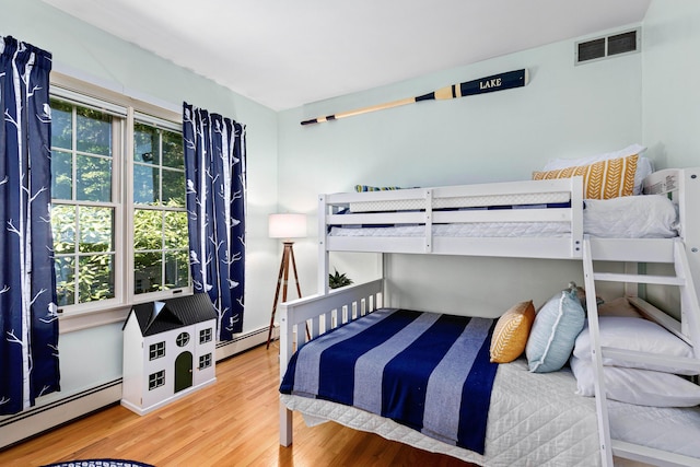 bedroom with baseboard heating, visible vents, and wood finished floors