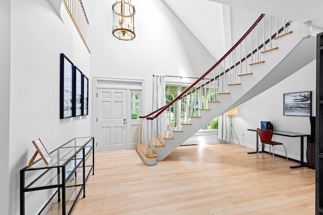 foyer with an inviting chandelier, stairs, baseboards, a towering ceiling, and wood finished floors