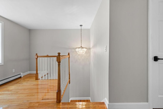 staircase featuring a baseboard heating unit, baseboards, wood finished floors, and a chandelier