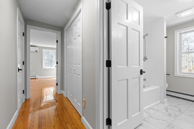 hallway featuring a baseboard heating unit, plenty of natural light, and an AC wall unit
