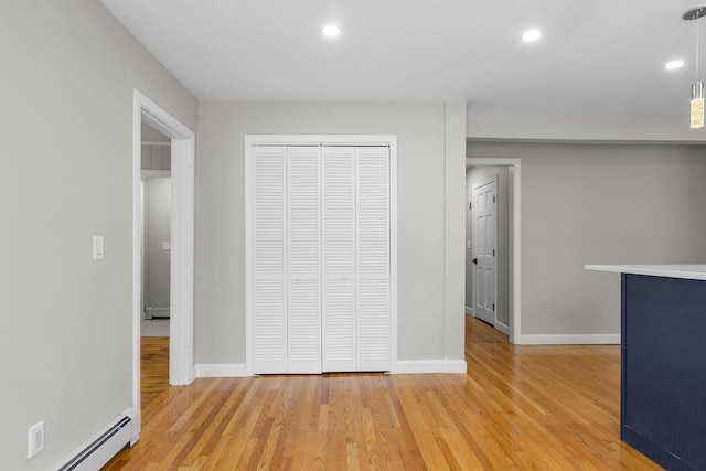 interior space with a baseboard heating unit, baseboards, a closet, and light wood-type flooring