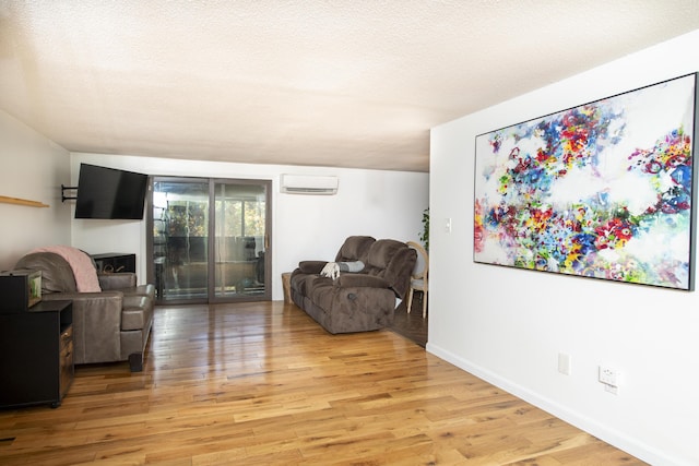 living room with a textured ceiling, light wood-type flooring, and a wall mounted air conditioner