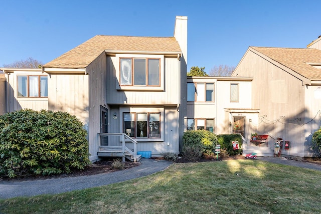 back of property featuring a shingled roof, a chimney, and a lawn