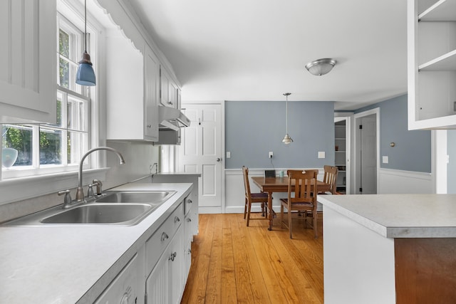 56 Wharf Ln, Yarmouth Port, MA 02675 - kitchen featuring light wood-type flooring, light countertops, a wainscoted wall, under cabinet range hood, and pendant lighting