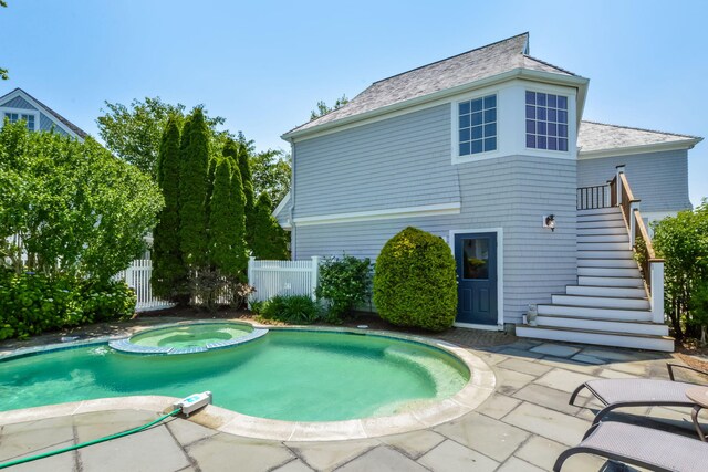 rear view of house with a patio area, stairs, a pool with connected hot tub, and fence