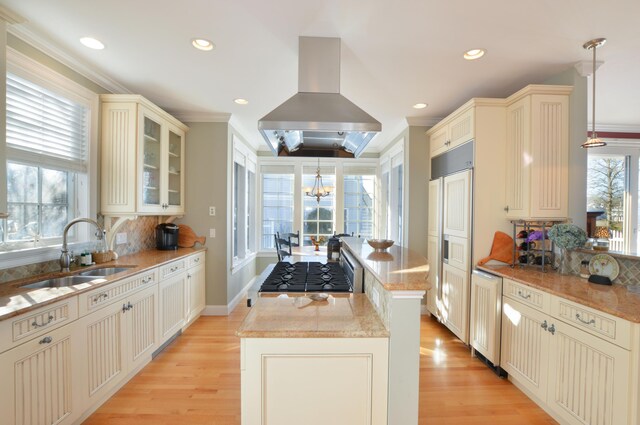 kitchen with island exhaust hood, cream cabinets, a center island, and a sink