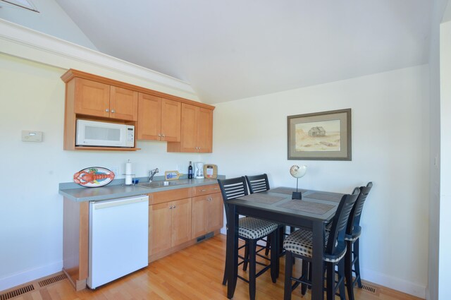 kitchen featuring vaulted ceiling, white appliances, a sink, light wood finished floors, and visible vents
