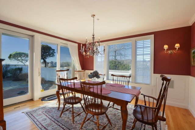dining space with ornamental molding, an inviting chandelier, light wood-style floors, and wainscoting