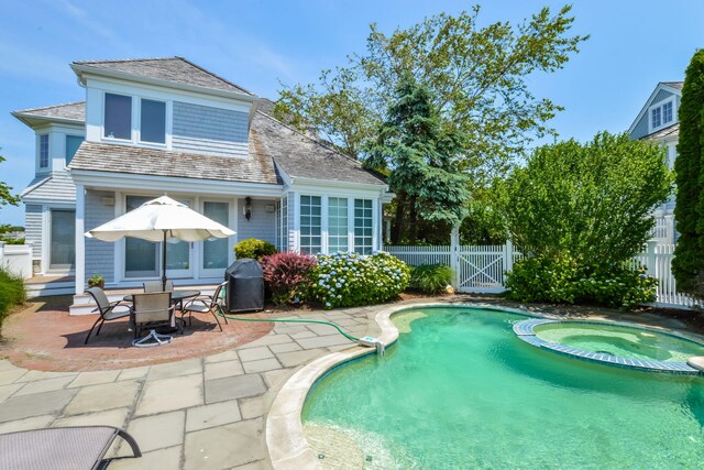 view of pool with fence, grilling area, a gate, a pool with connected hot tub, and a patio area