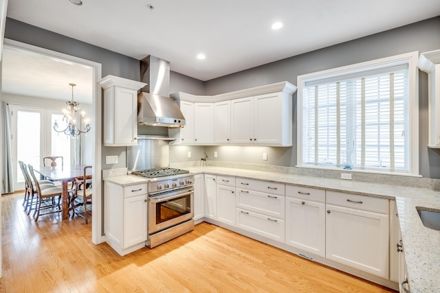 kitchen featuring stainless steel range with gas cooktop, wall chimney exhaust hood, white cabinetry, light wood-style floors, and recessed lighting