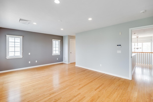 spare room featuring a smoke detector, a chandelier, light wood-type flooring, baseboards, and plenty of natural light