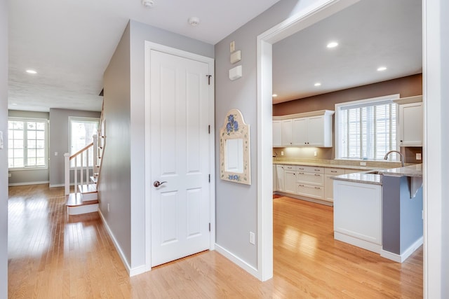 corridor featuring a sink, light wood-type flooring, baseboards, stairway, and recessed lighting