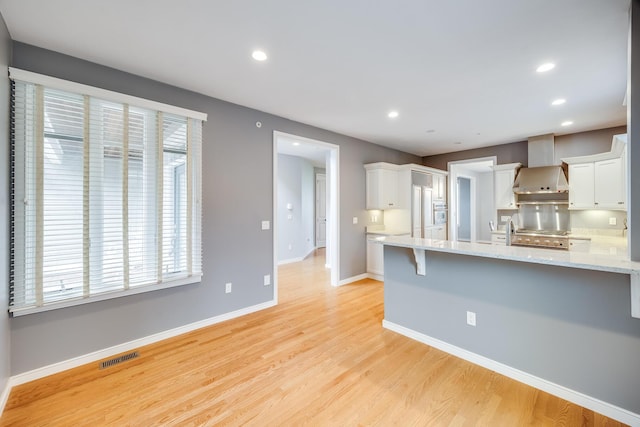 kitchen featuring wall chimney exhaust hood, white cabinetry, a peninsula, recessed lighting, and light wood-style floors