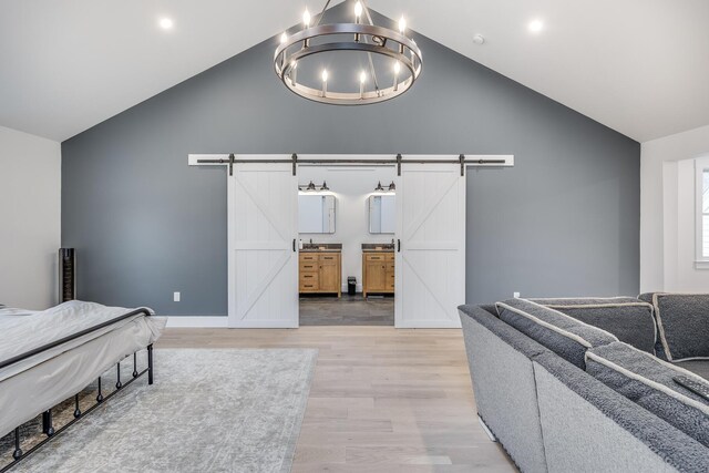 115 Kiahs Way E, Sandwich, MA 02537 - bedroom featuring a barn door, light wood finished floors, a chandelier, connected bathroom, and high vaulted ceiling