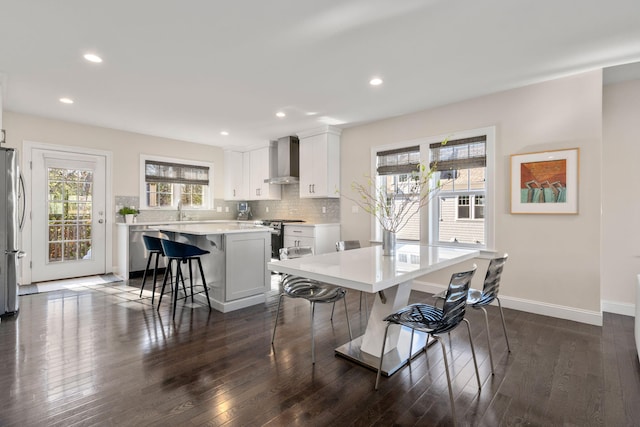 kitchen with a breakfast bar, a kitchen island, white cabinetry, light countertops, and wall chimney range hood