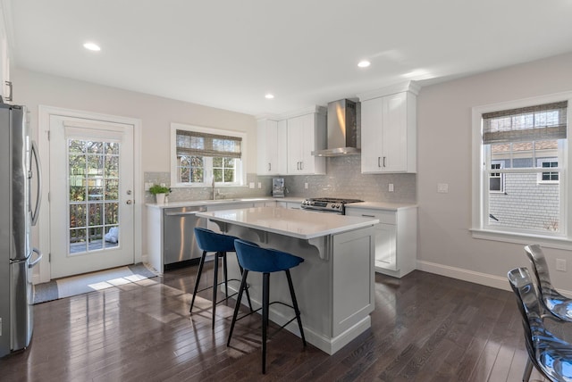 kitchen featuring wall chimney exhaust hood, a center island, stainless steel appliances, light countertops, and white cabinetry