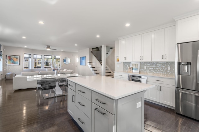 kitchen featuring white cabinets, open floor plan, a center island, stainless steel appliances, and light countertops