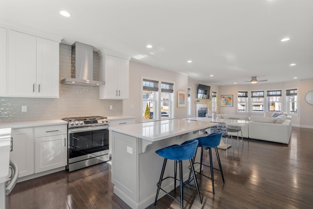 kitchen with stainless steel range with gas cooktop, light countertops, open floor plan, white cabinetry, and wall chimney exhaust hood