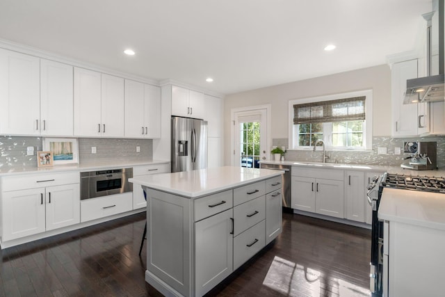 kitchen with stainless steel appliances, a sink, white cabinets, light countertops, and a center island