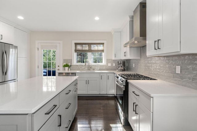 kitchen with a sink, white cabinetry, light countertops, appliances with stainless steel finishes, and wall chimney range hood