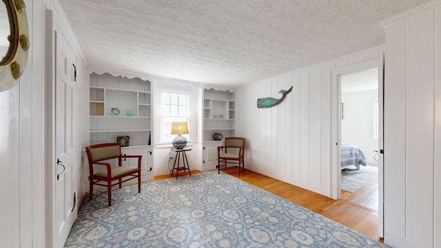 sitting room with wood walls, a textured ceiling, ornamental molding, and light wood-type flooring