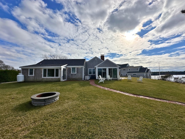 back of house featuring an outdoor fire pit, a yard, and a water view