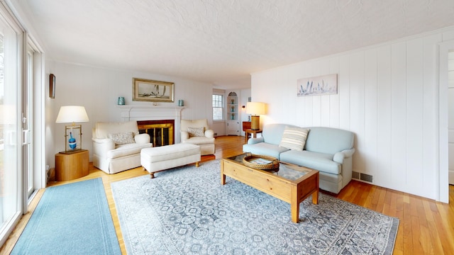 living room with a textured ceiling, light wood-type flooring, and wooden walls