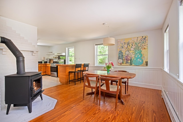 10 Bay View Rd, Wellfleet, MA 02667 - dining area featuring light wood finished floors, a baseboard radiator, a wood stove, and a wainscoted wall