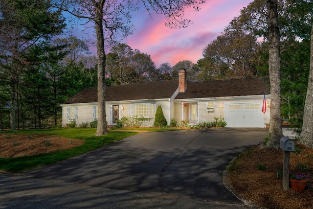 ranch-style house featuring driveway, an attached garage, a chimney, and a front lawn