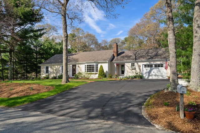 ranch-style house with driveway, an attached garage, a chimney, and a front lawn