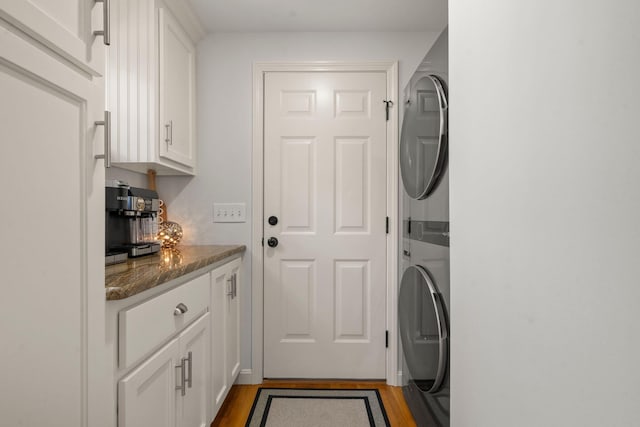 laundry area with stacked washing machine and dryer, wood finished floors, and cabinet space