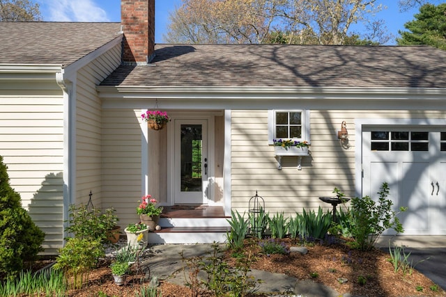 entrance to property with a garage, a chimney, and roof with shingles