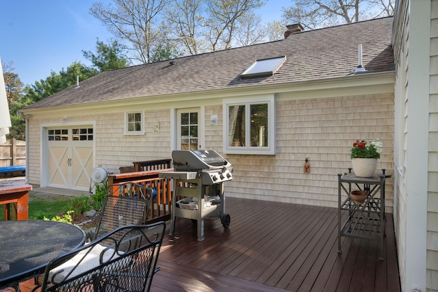 wooden deck featuring outdoor dining space, grilling area, and a garage